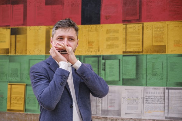 Man musician in a blue blazer and white sweater playing blues on a harmonica with eyes closed,