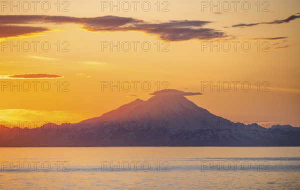 View of Cook Inlet on white mountain peaks of Mount Redoubt at sunset, picturesque golden light of