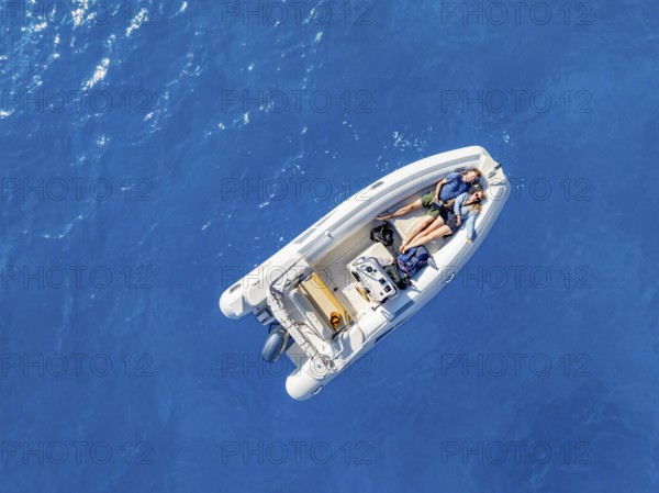 Young woman and young man lying in a motor boat on a blue sea, top-down, aerial view, Golfo di