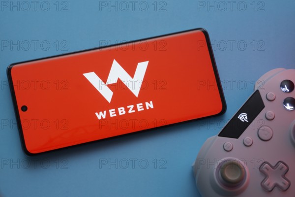 Dhaka, Bangladesh- 22 Mar 2025: Smartphone with Webzen logo, game controller, and earbuds on a