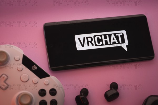 Dhaka, Bangladesh- 22 Mar 2025: Smartphone with VRChat logo, game controller, and earbuds on a pink