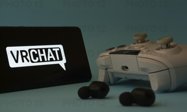 Dhaka, Bangladesh- 23 Mar 2025: A smartphone with a VRChat icon next to a controller and earbuds on