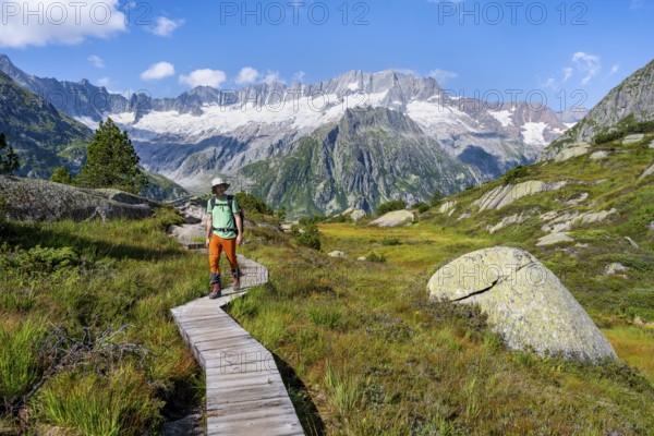 Mountaineers on wooden plank trail through mountain moor, in front of picturesque mountain scenery,