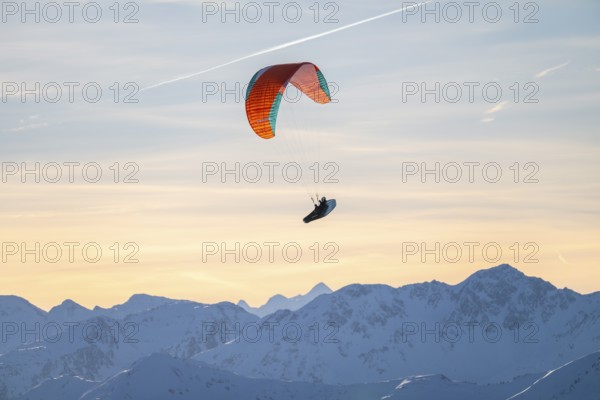 Paragliders flying over snowy mountain peaks in winter in evening light, Kitzbühel Alps, Tyrol,