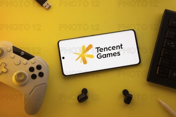 Dhaka, Bangladesh- 23 Mar 2025: Smartphone with Tencent Games logo, game controller, and earbuds on