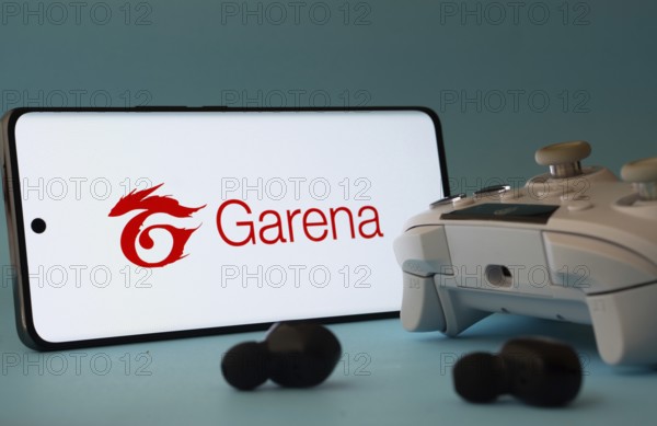 Dhaka, Bangladesh- 23 Mar 2025: A smartphone with a Garena icon next to a controller and earbuds on