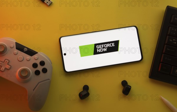 Dhaka, Bangladesh- 23 Mar 2025: Smartphone with Geforce Now logo, game controller, and earbuds on a