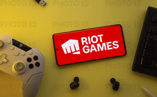 Dhaka, Bangladesh- 23 Mar 2025: Smartphone with Riot Games logo, game controller, and earbuds on a