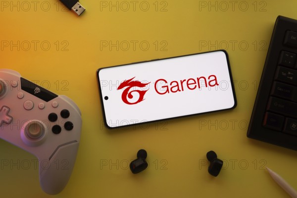 Dhaka, Bangladesh- 23 Mar 2025: Smartphone with Garena logo, game controller, and earbuds on a