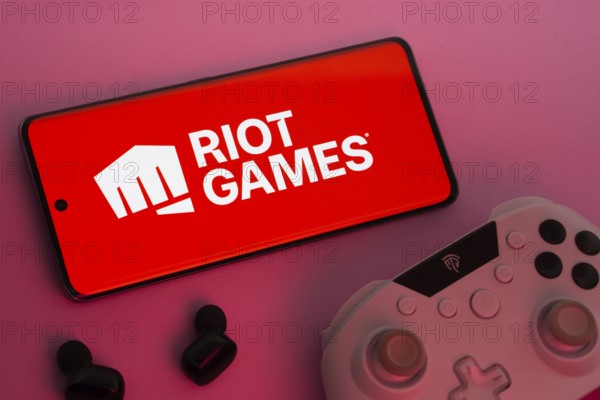 Dhaka, Bangladesh- 22 Mar 2025: Smartphone with Riot Games logo, game controller, and earbuds on a