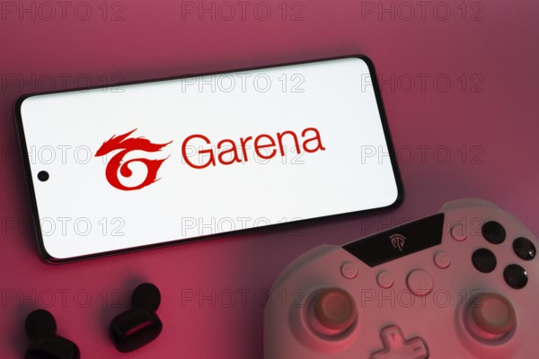 Dhaka, Bangladesh- 22 Mar 2025: Smartphone with Garena logo, game controller, and earbuds on a pink