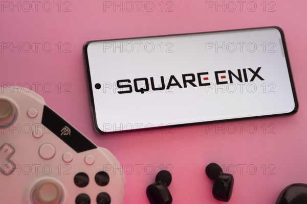 Dhaka, Bangladesh- 22 Mar 2025: Smartphone with Square Enix logo, game controller, and earbuds on a