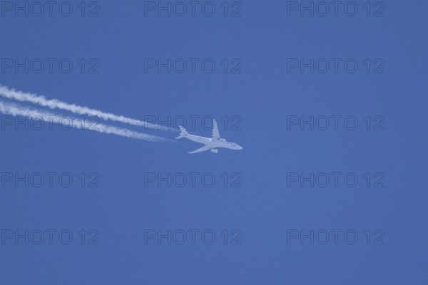 Jet passenger aircraft flying in a blue sky with contrails or vapour trails behind, England, United