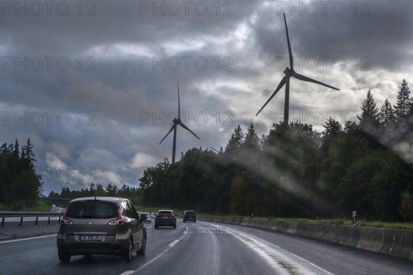 Tourist traffic on the A9 motorway during thunderstorms, wind turbines in the pine forest in the