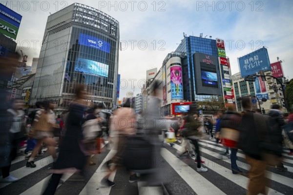 Crowd crossing zebra crossing on a large intersection, motion blur, back modern houses with