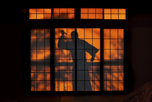 Shadow of a man, burglar with knife, assassin, ninja, on the balcony behind sliding shoji doors in