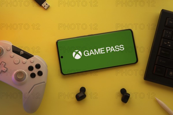 Dhaka, Bangladesh- 15 July 2025: Smartphone with Xbox game pass logo, game controller, and earbuds
