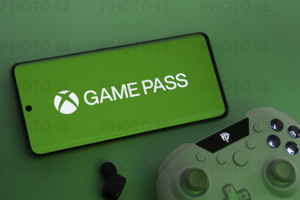 Dhaka, Bangladesh- 15 July 2025: Smartphone with Xbox Game Pass logo, game controller, and earbuds