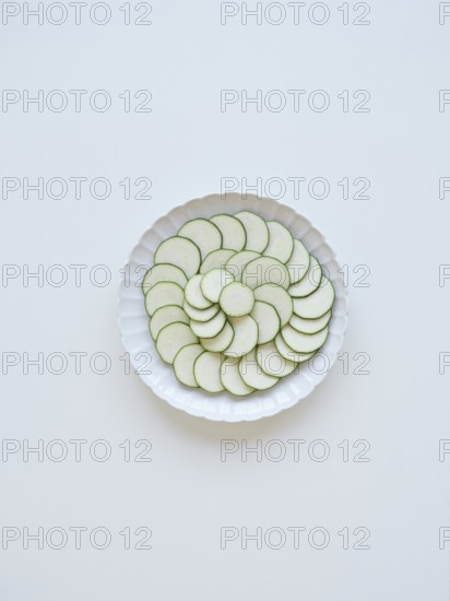Thinly sliced zucchini arranged on a white plate, forming a visually appealing pattern of