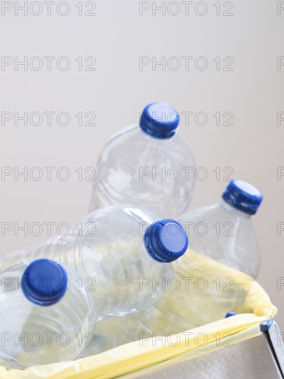 Empty plastic bottles with blue caps are being thrown away in trash can for recycling