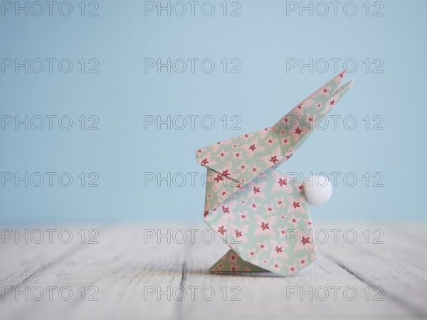 Floral origami easter bunny standing on a wooden table against a blue background