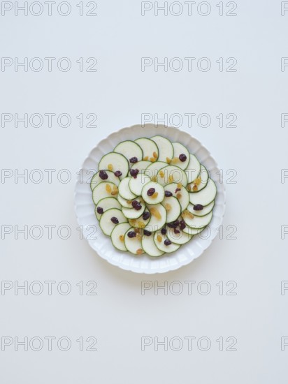 Thinly sliced zucchini arranged on a white plate, garnished with raisins and cranberries, creating