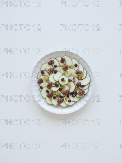 Sliced zucchini arranged on a white plate, creating a carpaccio with raisins and pecans, forming a