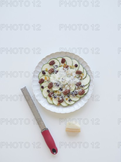 Delicious zucchini carpaccio with parmesan, pecan nuts, raisins, and grater on a white background,