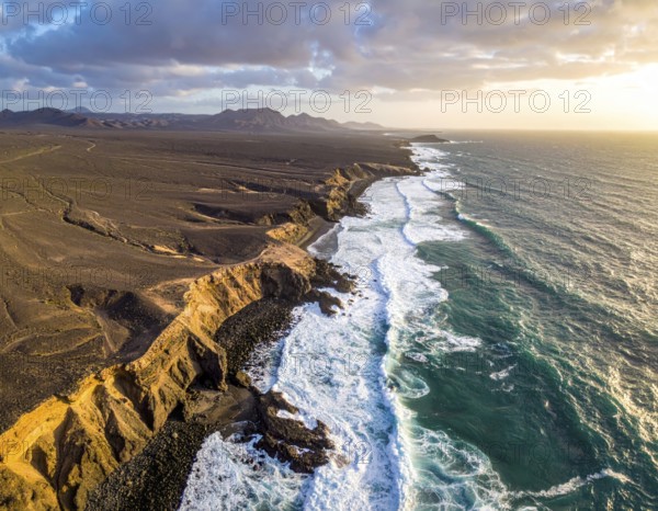 Desert landscape converges with ocean along a rugged coastal area, shore break at cliffs, blue