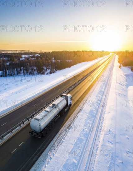 Petrol cargo truck lorry tanker driving on highway hauling oil products at sunrise, wide snowy