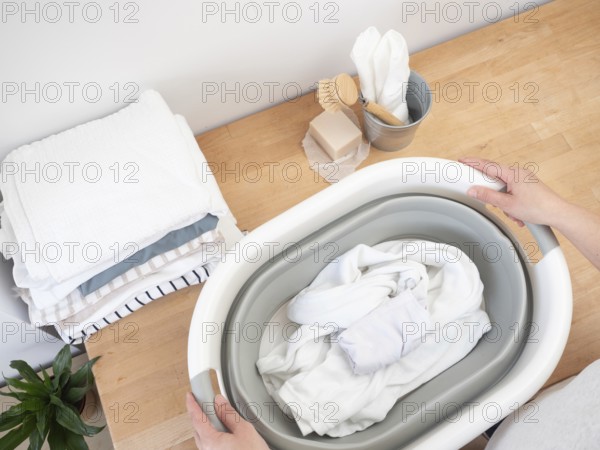Housekeeper holding a basin with white clothes, soap bar and brush on wooden table, preparing to