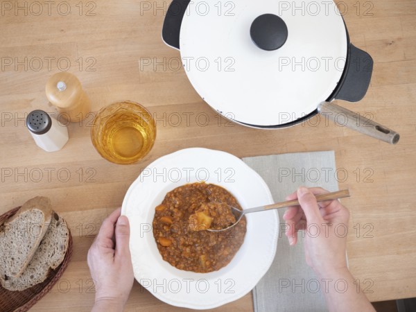 Woman eating a hearty lentil stew, served with whole wheat bread and a refreshing drink, creating a
