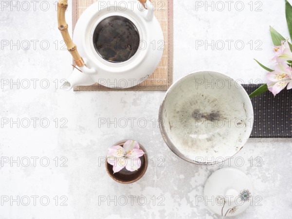 White teapot with bamboo handle, empty bowl, lid and pink flowers on light textured background are