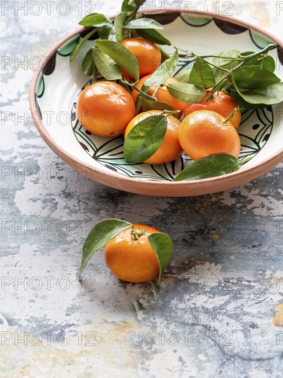 Vibrant tangerines with green leaves arranged in a decorative ceramic bowl, creating a rustic and
