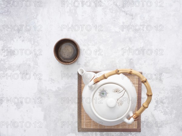 White teapot with bamboo handle and small wooden teacup on bamboo mat, ready for traditional asian