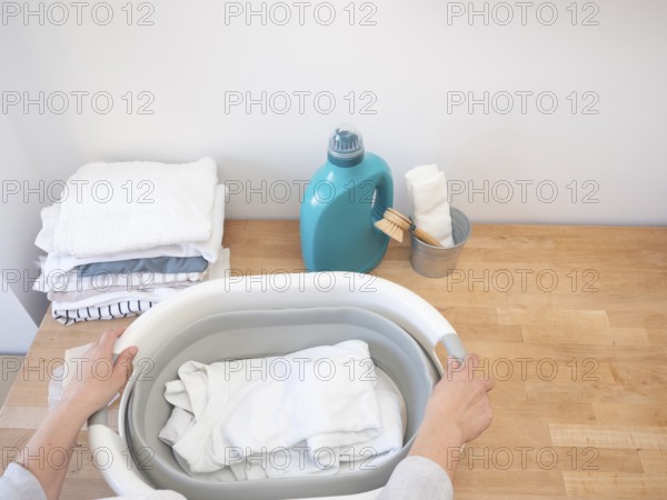 Woman holding laundry basket with clean white clothes, getting ready to do laundry with detergent