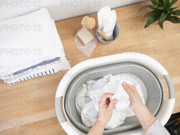 Woman soaking white clothes in bucket using natural soap and brush, promoting sustainable laundry