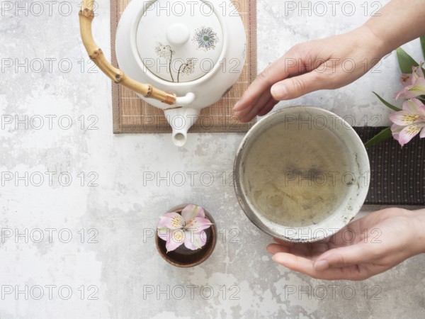 Woman gently holding a tea bowl during a traditional japanese tea ceremony, with teapot and flower