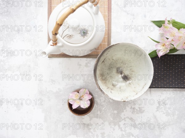 Asian tea ceremony arrangement with white teapot, empty bowl, pink flowers and bamboo placemat on