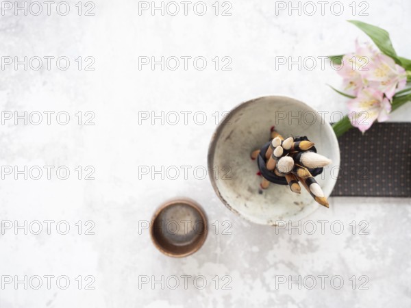 Calligraphy brushes tied with black ribbon in ceramic bowl near inkstone and pink flowers, ready