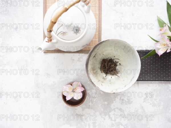 Traditional tea set with teapot, teacup, dried tea leaves, and pink alstroemeria flowers creates a