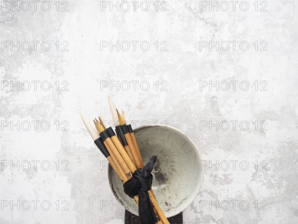 Multiple calligraphy brushes tied together with a black ribbon are resting on a ceramic bowl,