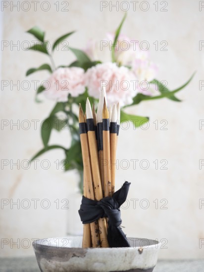 Calligraphy brushes are tied with a black ribbon and placed in a ceramic bowl, with pink carnations