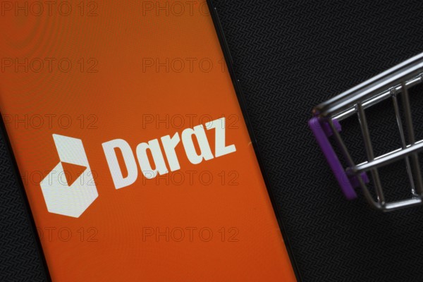 Dhaka, Bangladesh- 03 Oct 2025: A smartphone displaying the Daraz logo next to a miniature shopping