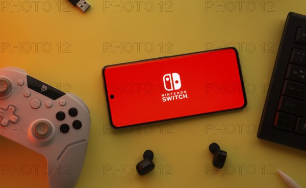 Dhaka, Bangladesh- 15 July 2025: Smartphone with nintendo switch logo, game controller, and earbuds
