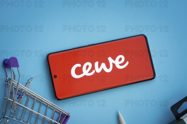 Dhaka, Bangladesh- 03 July 2025: Smartphone displaying Cewe logo with shopping cart on a blue