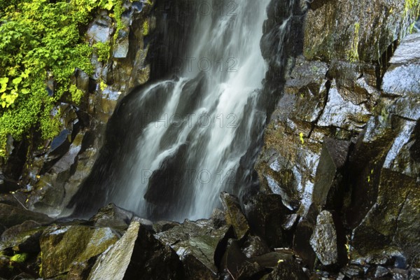 Vaucoux waterfall cascades gracefully over dark rocks, surrounded by lush greenery, Auvergne