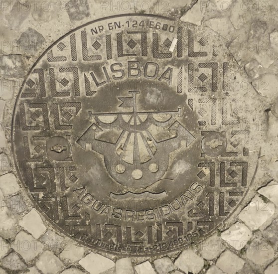 Engraved manhole cover on cobblestones with decorative patterns and a city coat of arms, Lisbon,