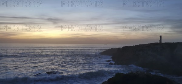 A lighthouse on the edge of the coast at sunset with waves in the sea, sunset over a peaceful ocean