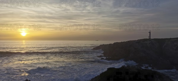 A lighthouse stands on cliffs in front of a sunset over the sea, hiking the Fisherman's Trail, Rota